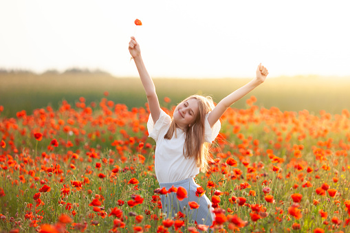 Blond girl stretching in the poppy field at sunrise. Start new day with happy smile. Unity with nature, natural cosmetics, good morning, relaxation, freedom and happiness concept.