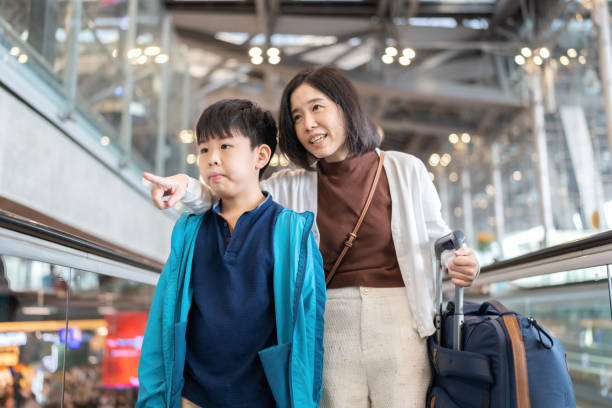 istock Explore experience by travel aboard. Mother and son standing on the escalator raising hand and point forward and son looking. Woman holding passport and luggage before going to check in counter at airport. Travel during holiday. 1482145774