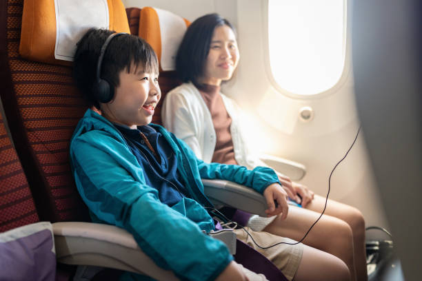 хорошее обслуживание в полете делает путешествие приятным. вид сбоку на азиатского мальчика в наушниках и куртке, сидящего с матерью в само - life jacket audio стоковые фото и изображения