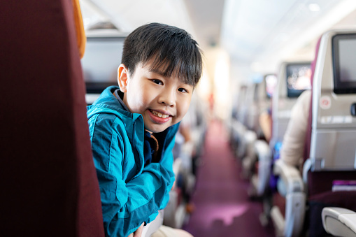 Tourism is an activity to build relationships within the family. Portrait of Asia boy sitting on the airplane and looking at camera during travel flight with smile. Kid enjoying to go aboard for travel with family during school holiday. Weekend activity with parent and make relationship.