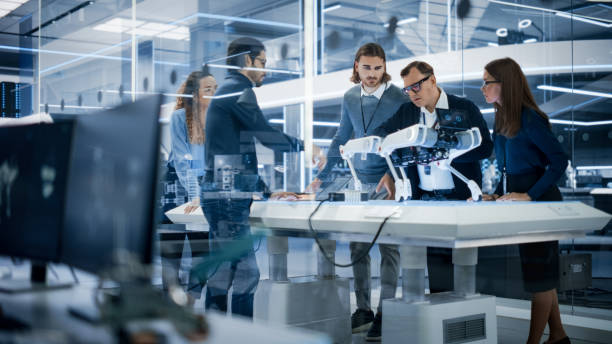 istock Diverse Team of Industrial Robotics Specialists Gathered Around a Table With a Mobile Robot. Scientists Use Tablet and Laptop Computers to Program the Automated AI Robotic Dog. 1482147421
