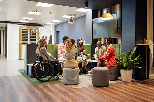 Full length view of relaxed group of colleagues in 20s, 40s, and 50s talking, sharing ideas, and laughing.