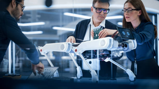 istock Diverse Team of Industrial Robotics Specialists Gathered Around a Table With a Mobile Robot. Scientists Use Tablet and Laptop Computers to Program the Automated AI Robotic Dog. 1482147470