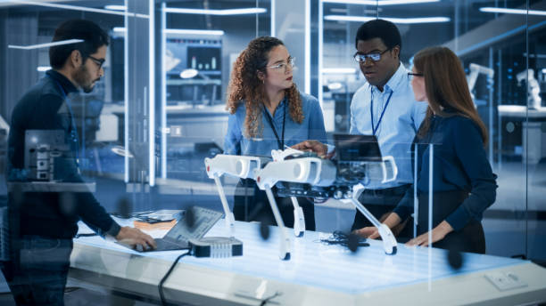 istock Diverse Team of Industrial Robotics Specialists Gathered Around a Table With a Mobile Robot. Scientists Use Tablet and Laptop Computers to Program the Automated AI Robotic Dog. 1482147498