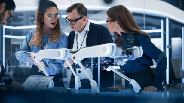istock Robotics Engineer, Project Manager and Machinery Operators Collaborate on a Robot Canine Project, Standing with Laptop Computer in Scientific Technology Lab. Young Team Developing an AI Robotic Dog. 1482148891
