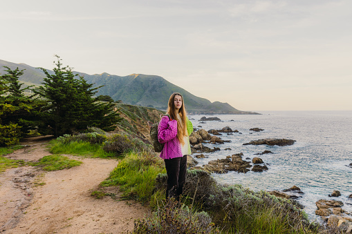 Side View of female with long hair wearing colourful knitted sweater exploring the scenic mountain coast of Monterey peninsula in the USA during sunny spring day