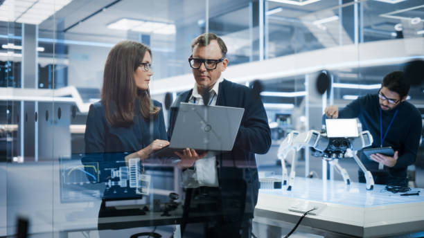 istock Chief Technology Officer Talking to Project Manager, Discussing Robot Dog Concept in High Tech Research and Development Facility. Professional Industrial Science Specialists Working in the Background. 1482153239