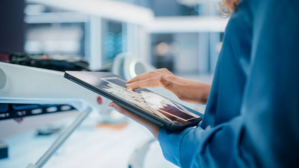 istock Close Up Footage of a Woman Using Tablet Computer in High Tech Modern Industrial Office Facility. Engineer Programming and Setting Up a Modern Robot Concept on a Smart Device. 1482153270