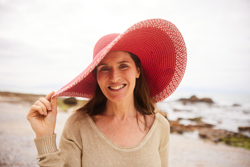 Portrait of smiling mature woman wearing a red sun hat while enjoying a day at the beach