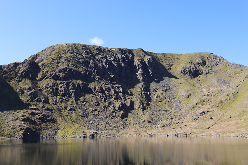 View of Helvellyn from Red Tarn on a sunny day with the mountain reflected in the lake beneath it