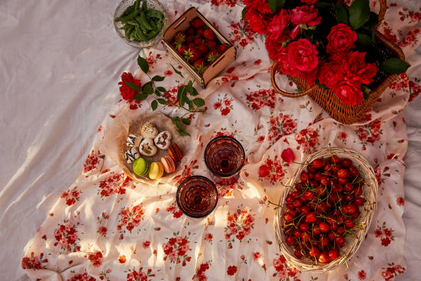 Summer aesthetic pink picnic with tablecloth marshmallows, macaroons, peas, strawberries, glasses of wine, cherries among pink roses in the garden. Romantic dinner