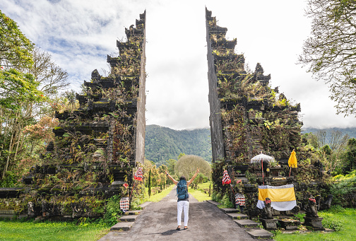 Traveller man with backpack posing in front of  Handara gate, traditional Balinese Architecture, View of Landmark Temple Gates in Northern Bali, Indonesia in Bali, Indonesia.