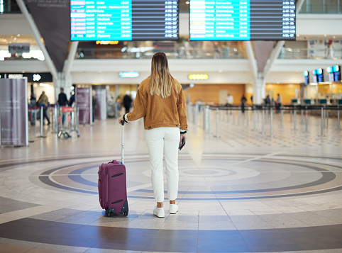 Woman, airport and luggage checking flight times for travel, vacation or journey with passport in Cape Town. Female traveler standing and waiting ready for departure, boarding plane or immigration