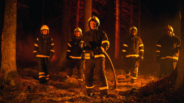 istock Diverse Brigade of Five Professional Firefighters Posing and Looking at Camera in a Forest Fire Situation. Multicultural Team Wearing Protective Clothing and Gear. Squad Leader Holding a Firehose. 1482173885