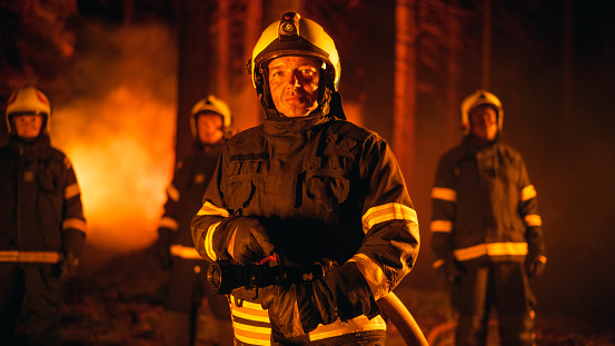 Diverse Male and Female Team of Professional Firefighters Standing in a Smoked Out Forest During a Wildland Fire, Posing and Looking at Camera. Group Wearing Protective Clothing, Helmets and Gear.