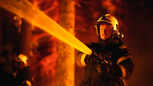 istock Focused Brave Professional Firefighter Using a Firehose to Fight a Raging Dangerous Forest Fire. Experienced Fireman Skillfully Manages a Stressful Situation and Stays Protected. 1482174198