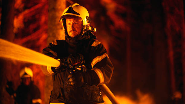 istock Focused Brave Professional Firefighter Using a Firehose to Fight a Raging Dangerous Forest Fire. Experienced Fireman Skillfully Manages a Stressful Situation and Stays Safe. 1482174213