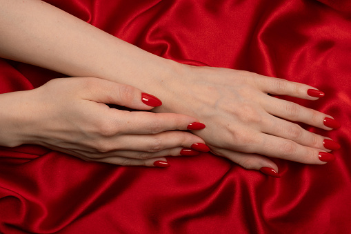 Beautiful red manicure on woman hands on a luxury red silk backround.