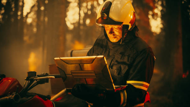 istock Portrait of a Fireman in Safety Gear Using Heavy-Duty Laptop Computer, Reporting on a Situation with a Dangerous Wildland Fire in a Forest. Hard Day at Work for a Brave Firefighter Volunteer. 1482174596