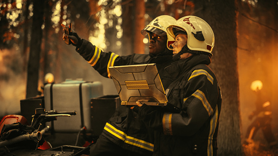 Portrait of Female and Male Professional Firefighters Standing Next to an All-Terrain Vehicle, Using Laptop Computer and Figuring Out a Best Strategy for Extinguishing the Wildland Fire.