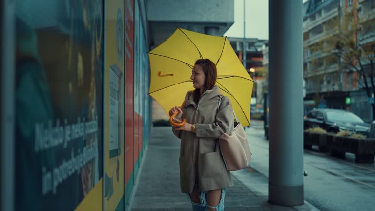 Young woman window shopping with a yellow umbrella on a rainy day