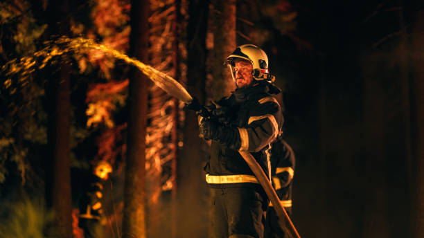 istock Experienced Firefighter Extinguishing a Wildland Fire Deep in a Smoke-Filled Forest. Professional in Safety Uniform and Helmet Using a Firehose to Battle Dangerous Fire. 1482177608