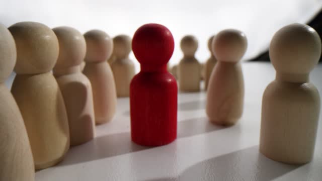 Red figurine stands between long rows of wooden figures