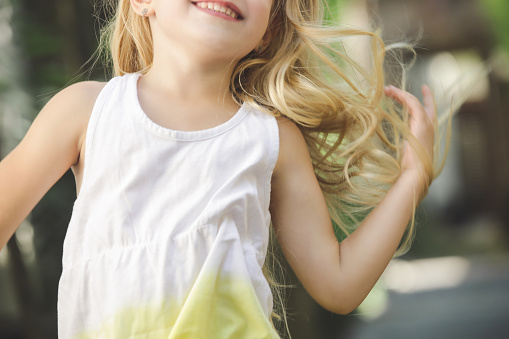 Close up of happy little girl with long hair jumping and laughing in the park