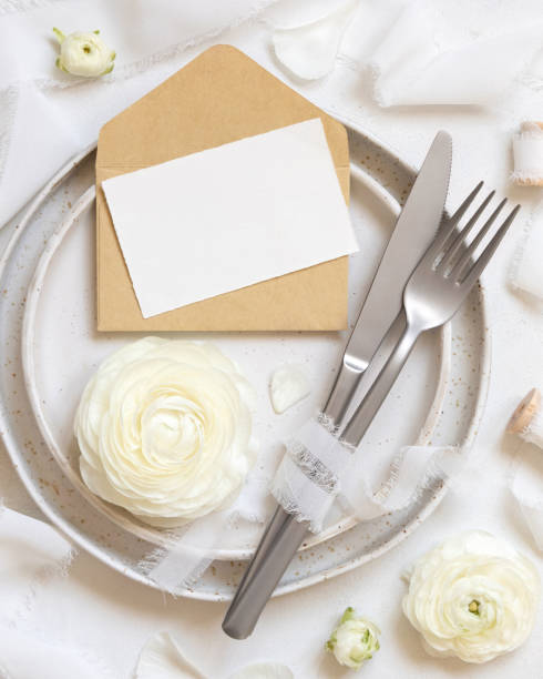 istock Wedding table setting with card and envelope near cream roses and white silk ribbons top view, mockup 1482183622