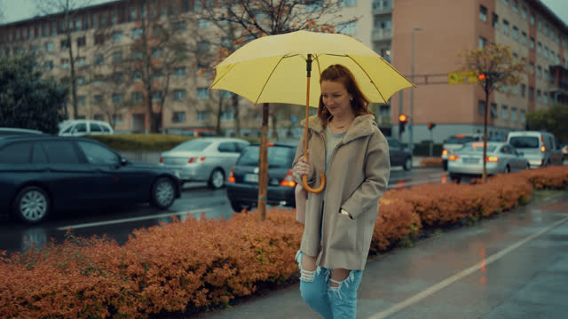 Freckled young woman walks with a yellow umbrella in the city on a rainy day