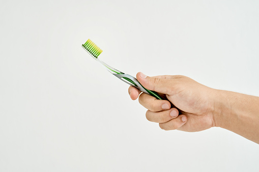 Close-up of an unrecognizable young man holding up a toothbrush against a white background