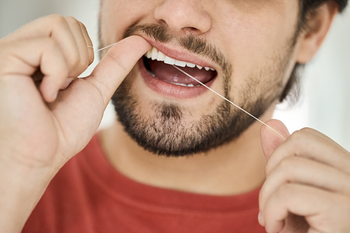 Close-up shot of a young man using a floss to completely clean his teeth
