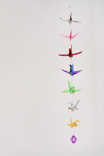 String of multi colored origami cranes hanging on in row against a white background
