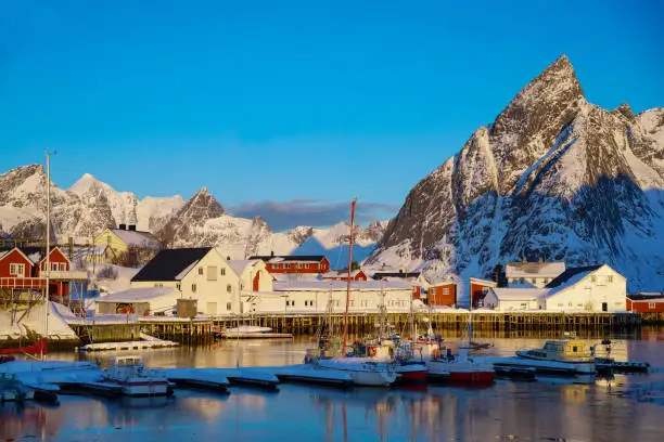 Morning sun on fishing village of Hamnøy on the Lofoten Islands with mountain range covered with snow and blue sky in the background during late winter. Northern Norway.