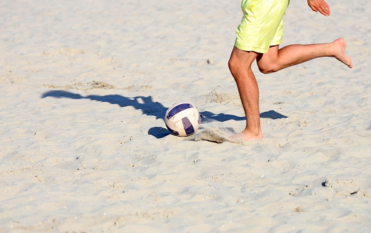 Playing football or soccer on the beach with friends, vacation.