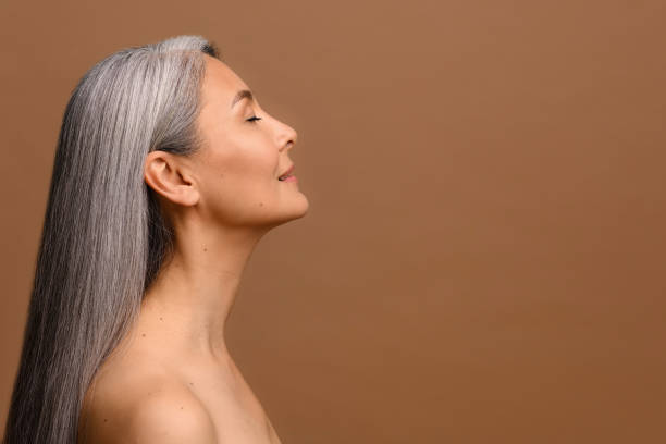 Charming middle-aged woman with naked shoulders stands in profile stock photo