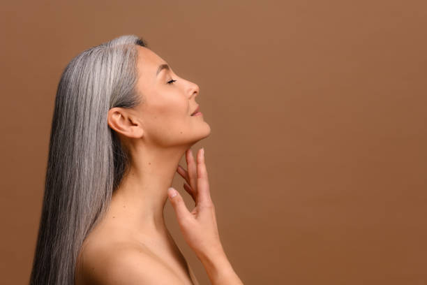 Side view at enchanting topless middle aged Asian woman isolated on brown background stock photo
