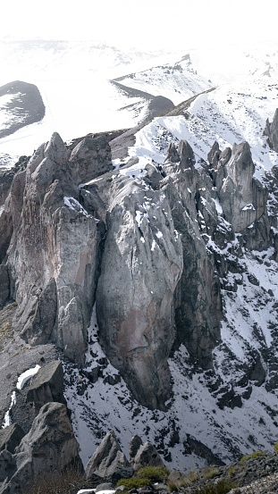 A vertical photograph of a majestic snow-capped mountain, taken from a low angle to capture the full scale and grandeur of the peak