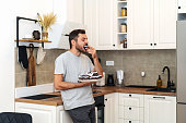 Man stands in kitchen holds plate of sweets eating muffin.