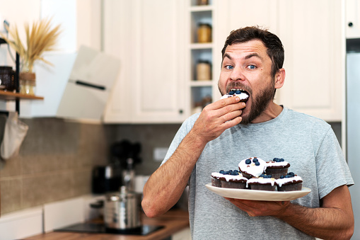 Hungry man eating homemade cupcakes in kitchen.