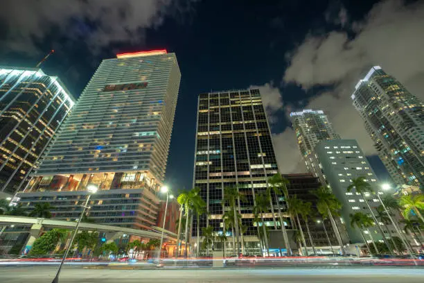 Downtown district of of Miami Brickell in Florida, USA. Brightly illuminated high skyscraper buildings and street with car trails and metrorail traffic in modern american midtown.