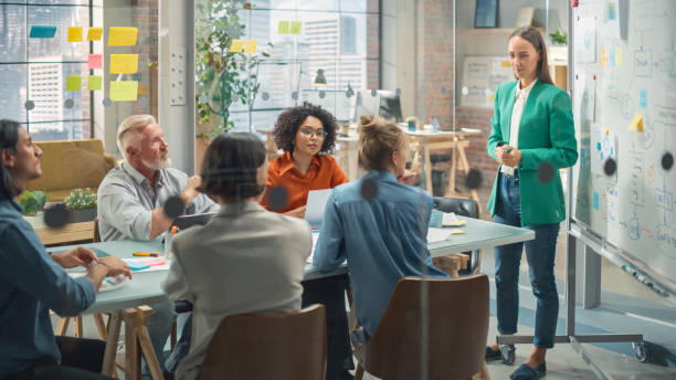 istock Collaborative Multiethnic Team Group Attending a Meeting to Develop a Strategy. Young Female Manager Using a Whiteboard to Explain Plan Steps. Colleagues Following her Presentation 1482197152