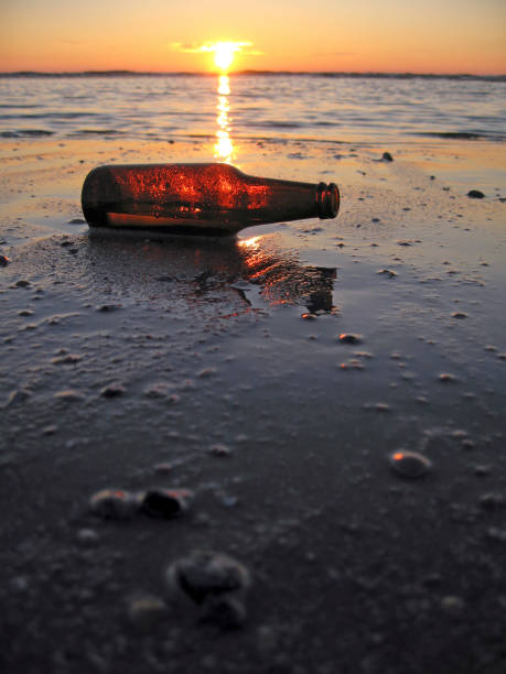 Empty glass bottle lying in the sea at the beach at sundown