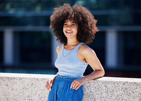 Portrait, fashion and city with a black woman outdoor on a bridge, looking relaxed during a summer day. Street, style or urban and an attractive young female posing outside with an afro hairstyle