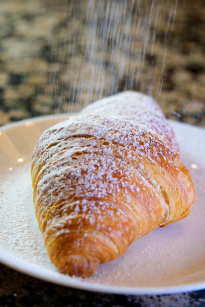 Fluffy stuffed croissants sprinkled with powdered sugar in slow mo. Close-up pastries are decorated with powdered sugar. Homemade delicious pastries. Puff pastry and buns with sweet filling.