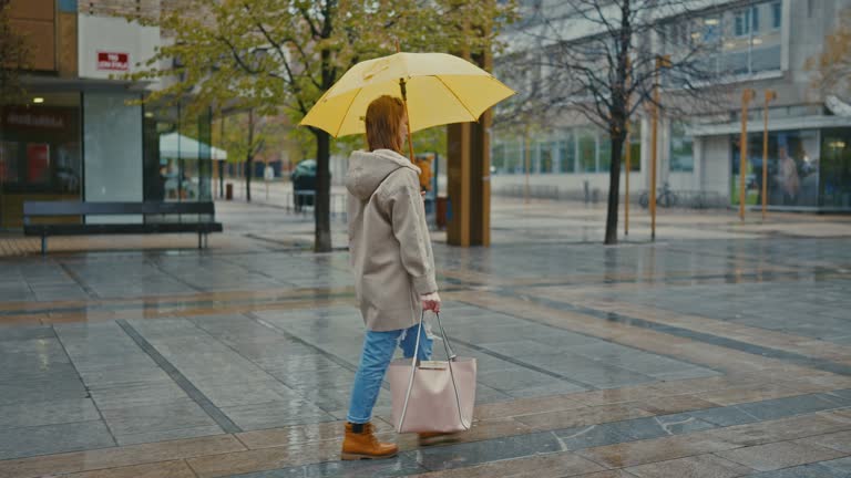 SLO MO Young woman walks with a yellow umbrella in the city on a rainy day