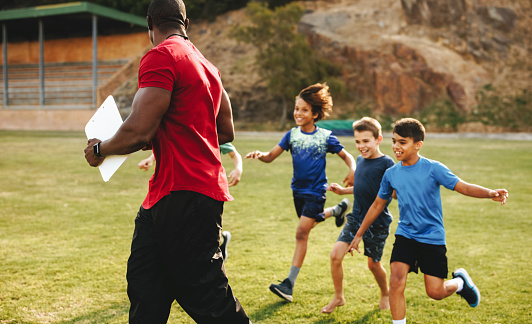 Sports coach getting chased by his sports team. School sports team running to thier coach. Coach and students being playful on the sports field.