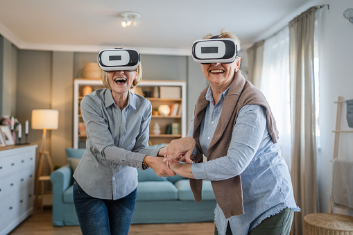 two women mature senior caucasian females old mother and daughter at home enjoy virtual reality VR headset active senior concept copy space
