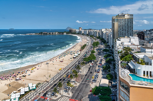 This photo captures the vibrant atmosphere of Copacabana Beach in Rio De Janeiro, Brazil. With its pristine white sand stretching along the azure waters of the Atlantic Ocean, this iconic beach is a magnet for tourists and locals alike. The photo showcases the beach's bustling boardwalk lined with palm trees, beach umbrellas, and colorful tents where visitors can enjoy snacks and drinks. This photo is perfect for travel brochures, websites, or any project that aims to capture the beauty and energy of one of the world's most famous beaches.