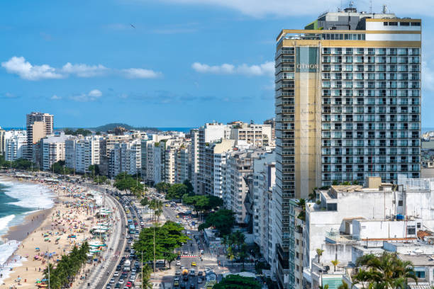 This photo captures the vibrant atmosphere of Copacabana Beach in Rio De Janeiro, Brazil. With its pristine white sand stretching along the azure waters of the Atlantic Ocean, this iconic beach is a magnet for tourists and locals alike. The photo showcases the beach's bustling boardwalk lined with palm trees, beach umbrellas, and colorful tents where visitors can enjoy snacks and drinks. This photo is perfect for travel brochures, websites, or any project that aims to capture the beauty and energy of one of the world's most famous beaches.